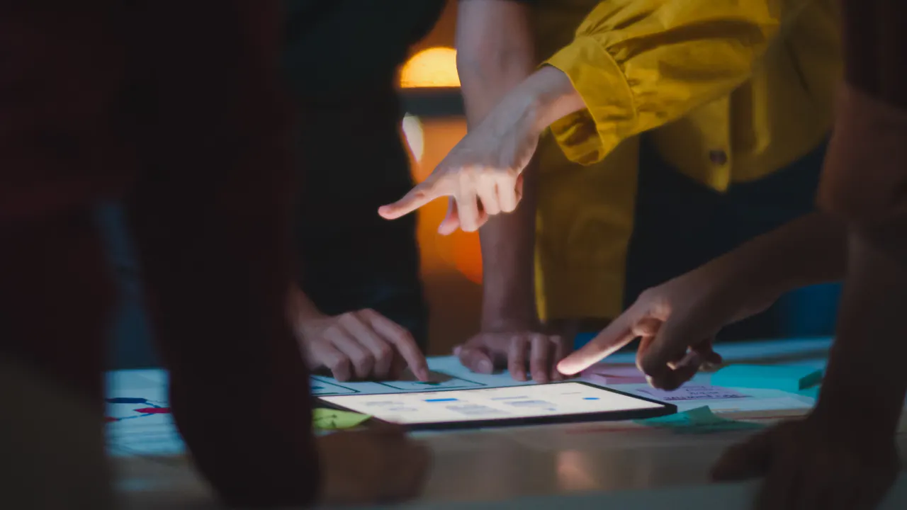 Colleagues tapping a tablet together at a table, illustrating interactive content that engages an audience