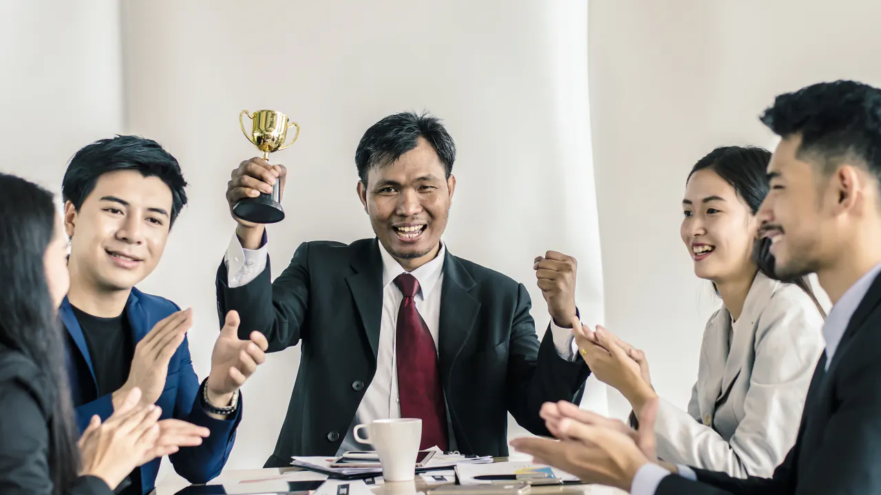 Business team applauding a colleague holding a trophy, illustrating GenSales awards and recognition