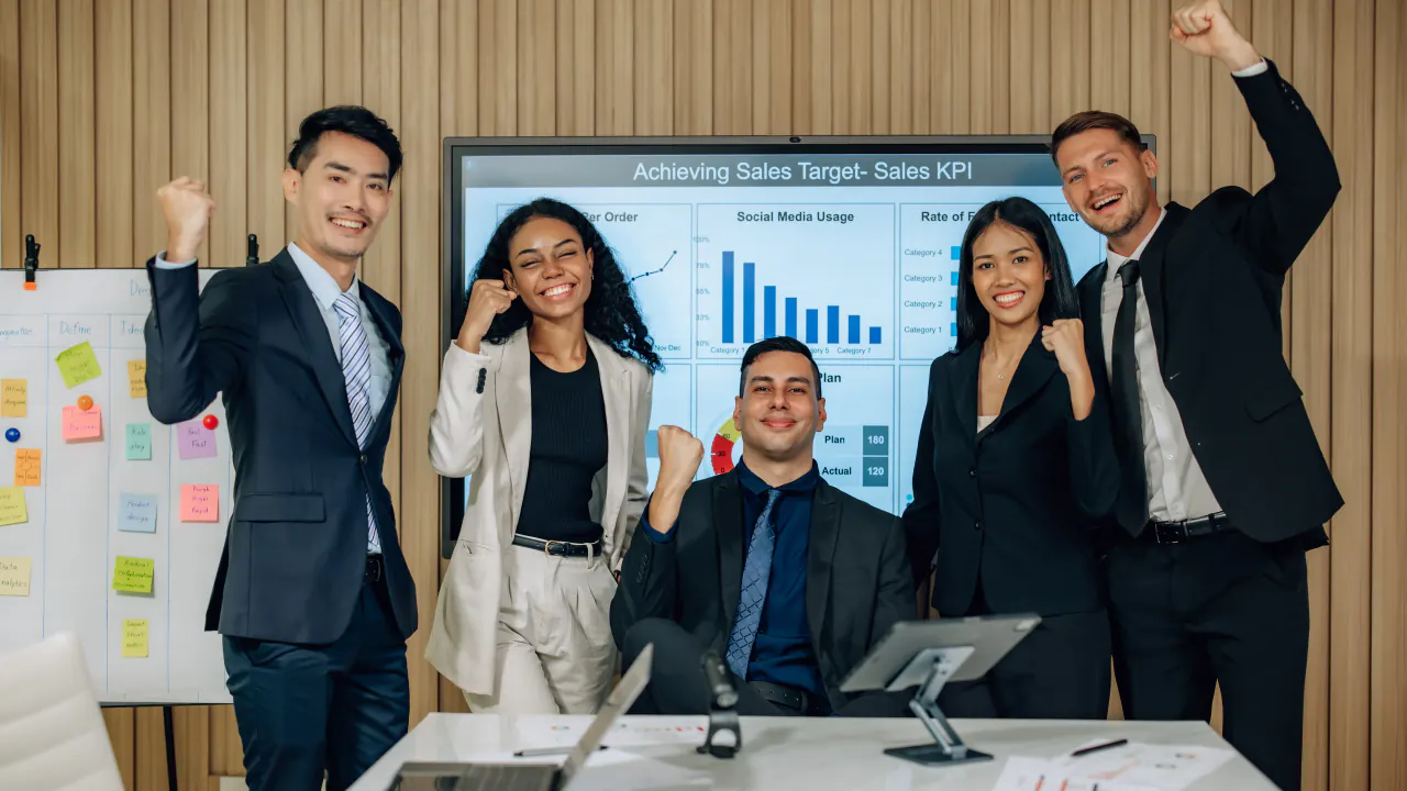 Five business colleagues cheering in front of a sales KPI screen, representing lead generation services for B2B growth