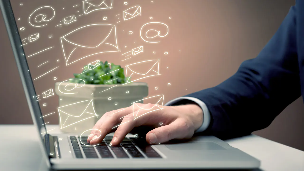 Hand typing on a laptop with email icons above the keyboard, illustrating B2B lead nurturing