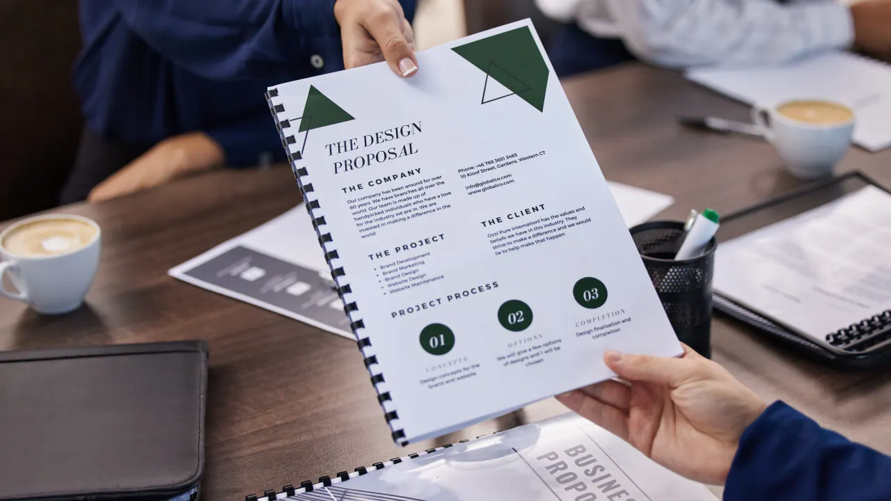 Hands passing a printed business proposal across a desk, illustrating how to write a strong business proposal