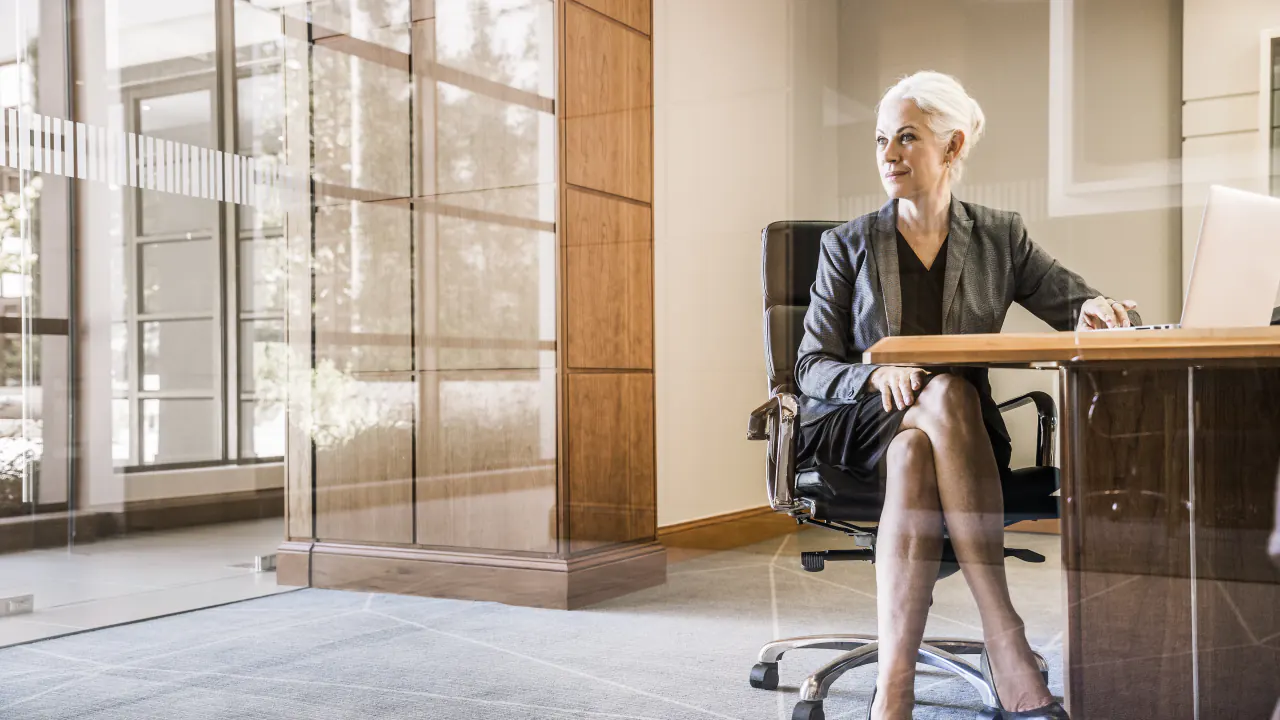 Executive woman sitting at her desk in a glass office, illustrating how to reach C-level executives