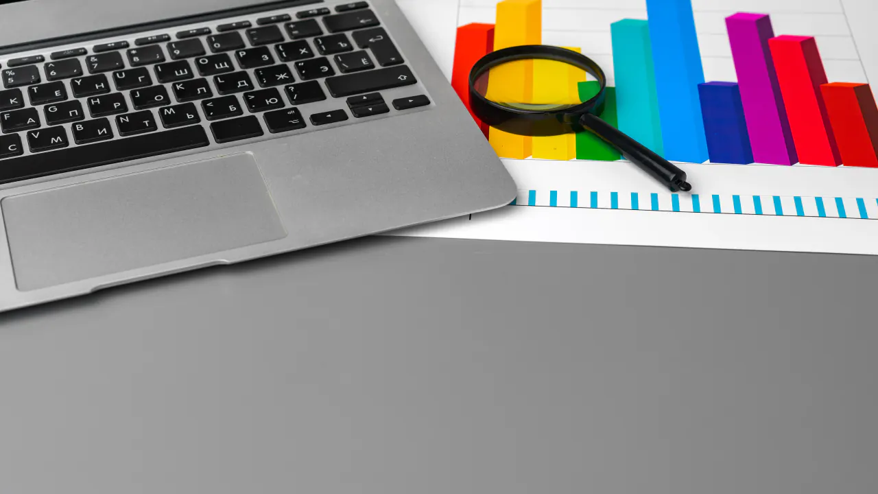 Laptop with a magnifying glass over colorful bar charts, illustrating competitor website analysis
