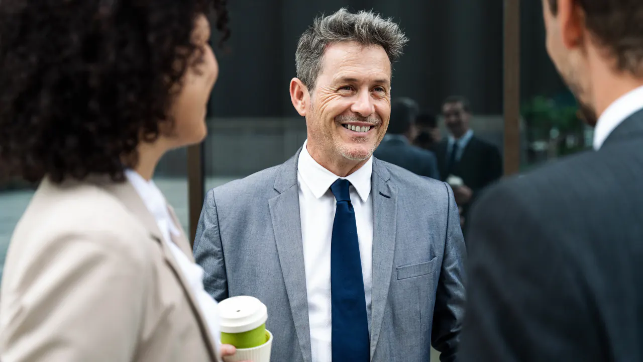 Smiling salesman chatting with colleagues at a networking event, illustrating conversation starters for salespeople