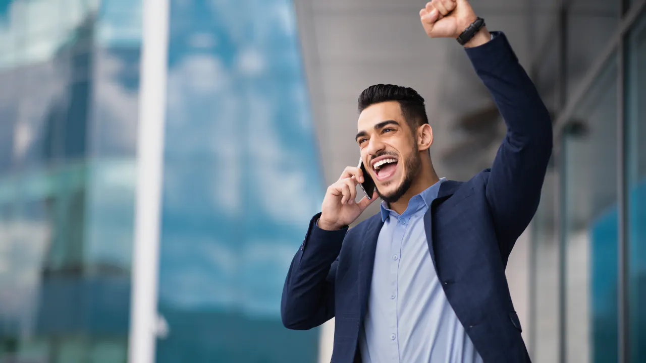 Excited businessman raising a fist during a phone call, illustrating conversion rate in cold calling