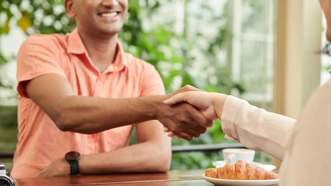 Two professionals shaking hands over coffee, illustrating customer acquisition