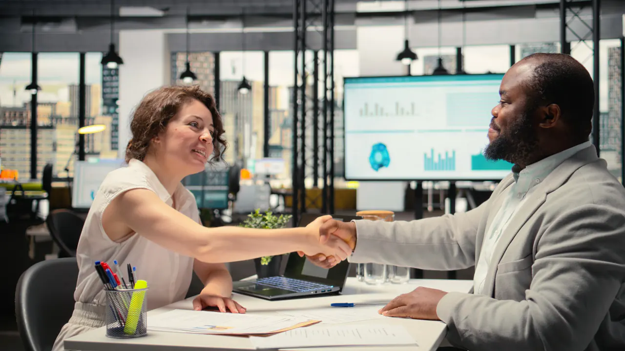Customer success manager shaking hands with a client at a desk, illustrating customer success