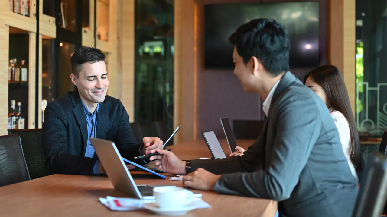 Two professionals talking over laptops in a meeting, illustrating discovery questions for sales calls