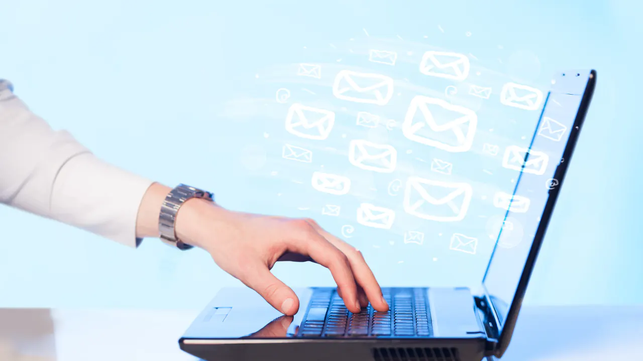 Hand typing on a laptop with email icons floating above, illustrating follow-up email templates after no response