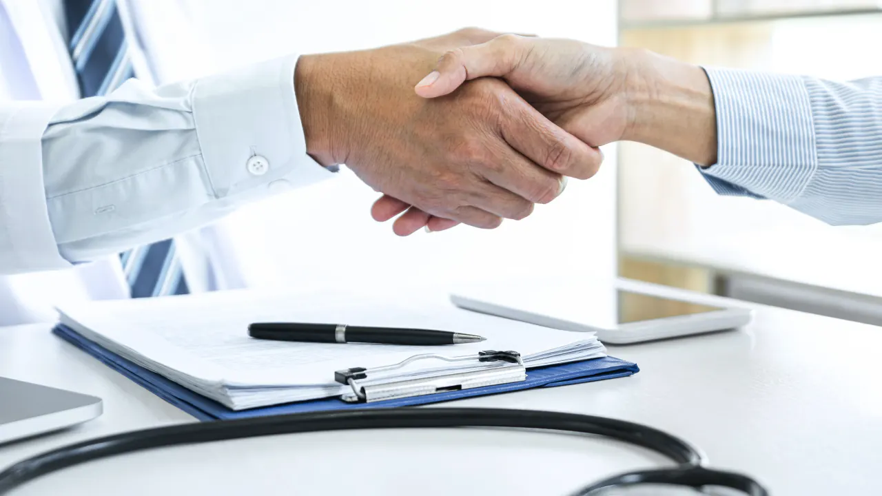 Handshake over a clipboard and stethoscope, illustrating outsourced B2B SDR services for healthcare companies
