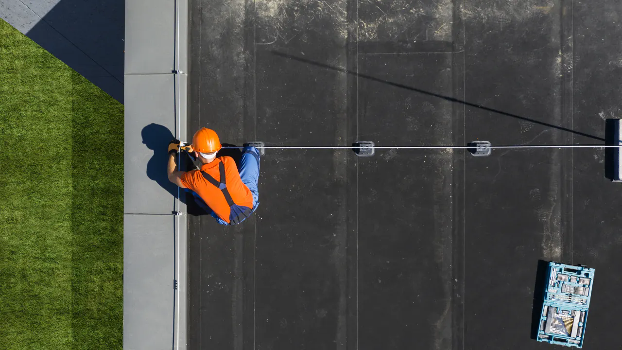 Aerial view of a roofer in a safety harness on a flat roof, illustrating lead generation for commercial roofers