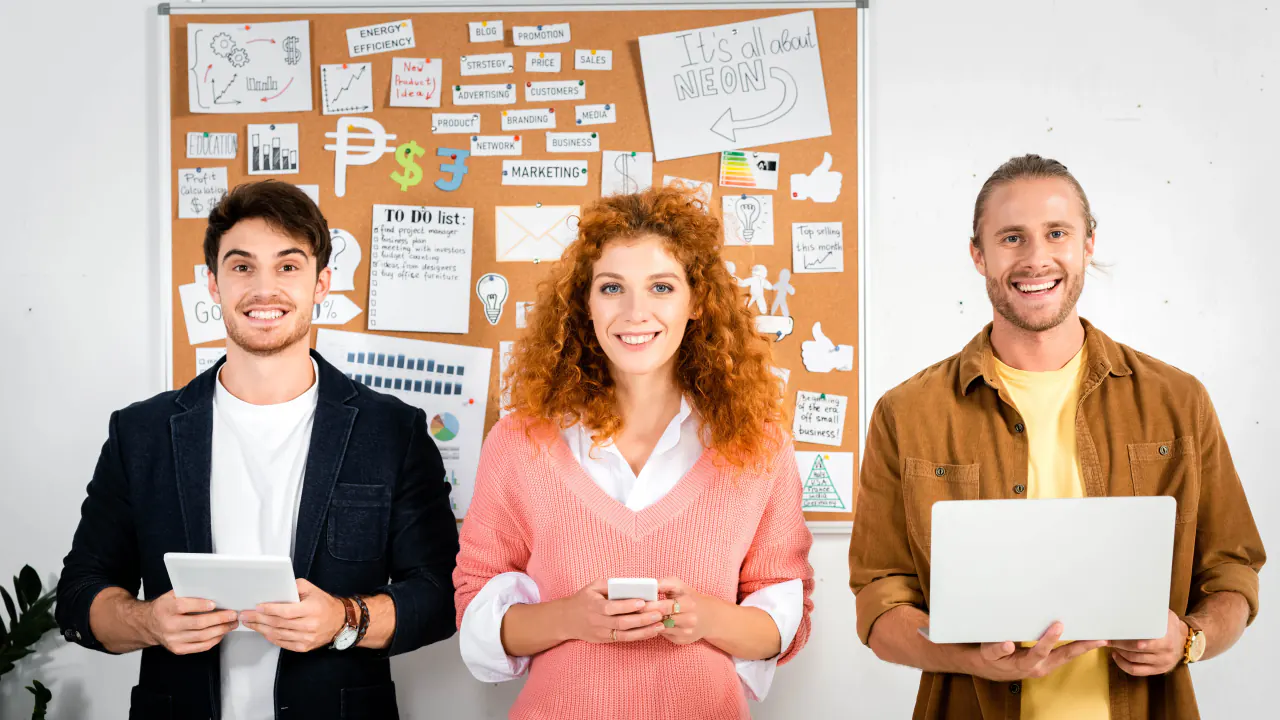 Three smiling colleagues with devices in front of a planning board, illustrating lead gen marketing tactics