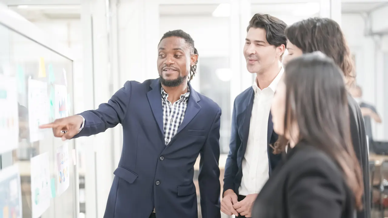 Sales manager pointing at a planning board while briefing colleagues, illustrating B2B lead generation