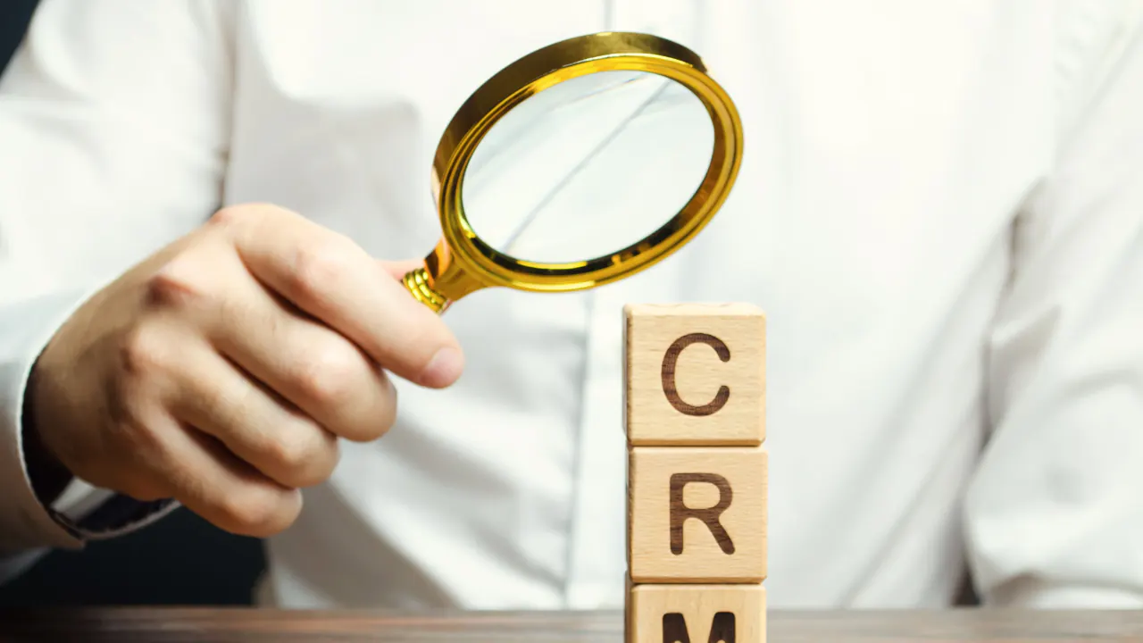 Hand holding a magnifying glass over CRM letter blocks, illustrating lead management