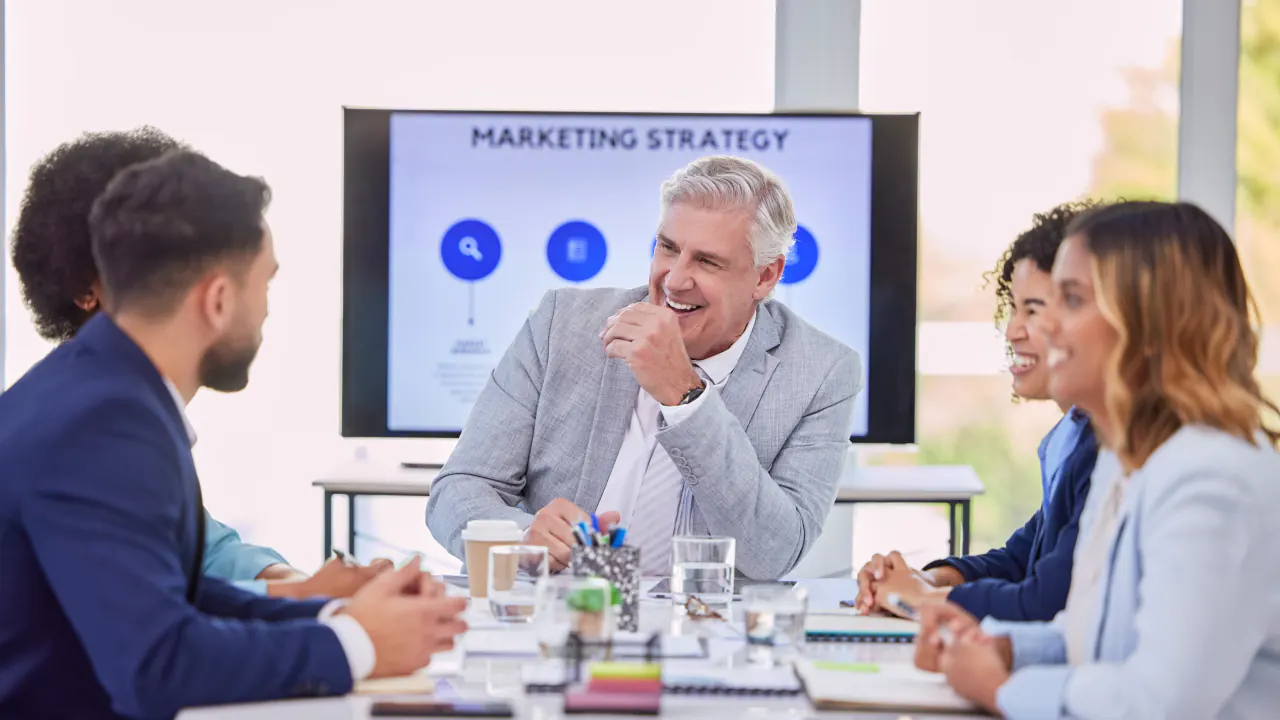 Sales team meeting around a table with a marketing strategy presentation, illustrating the MEDDIC sales process
