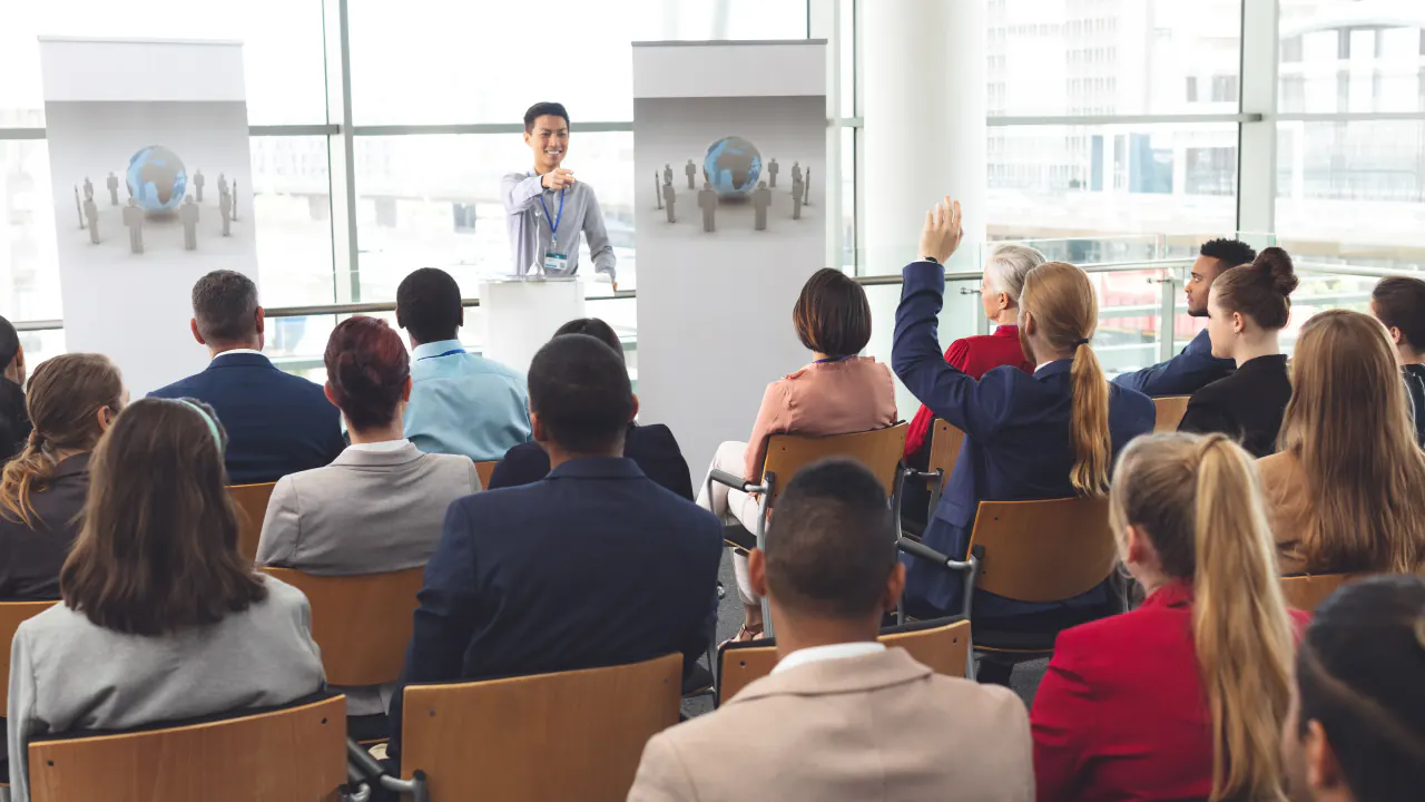 Speaker presenting to a seated audience at a seminar, illustrating the Miller Heiman sales process