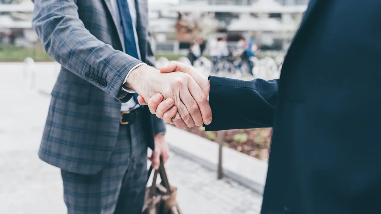 Two businessmen shaking hands outdoors, illustrating a sales opportunity