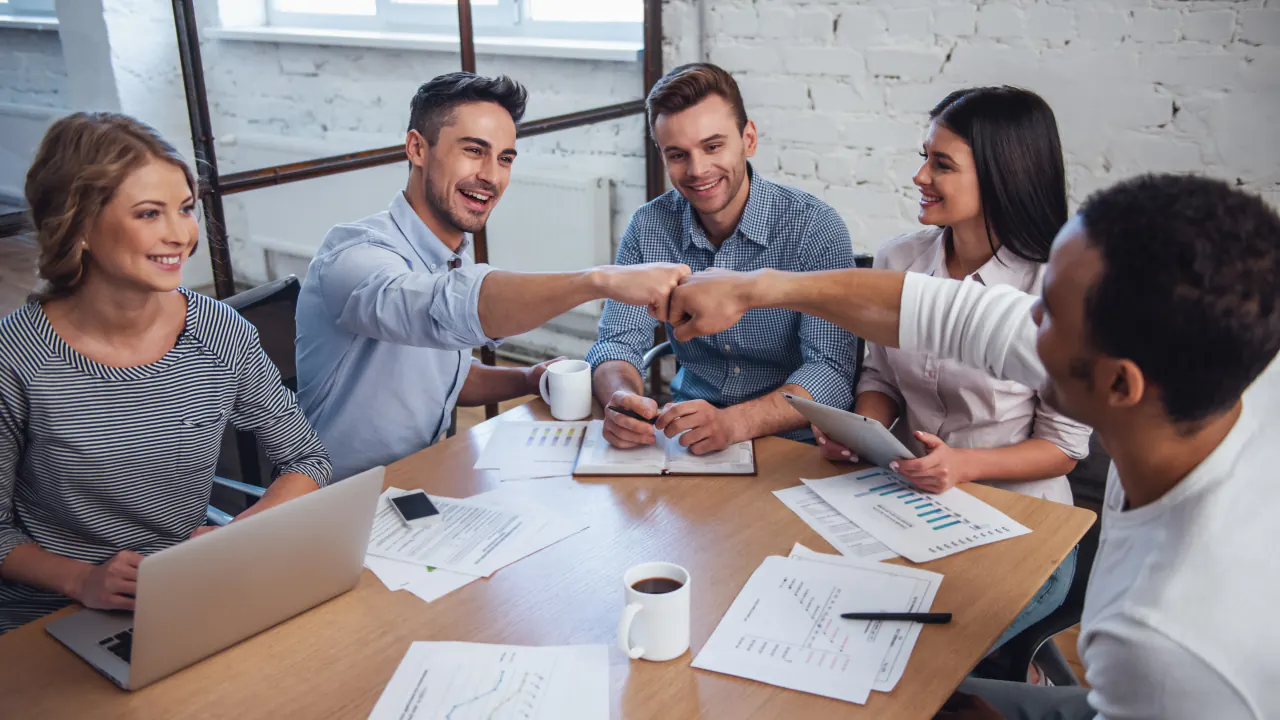 Team fist-bumping around a meeting table, illustrating outsourced sales and marketing