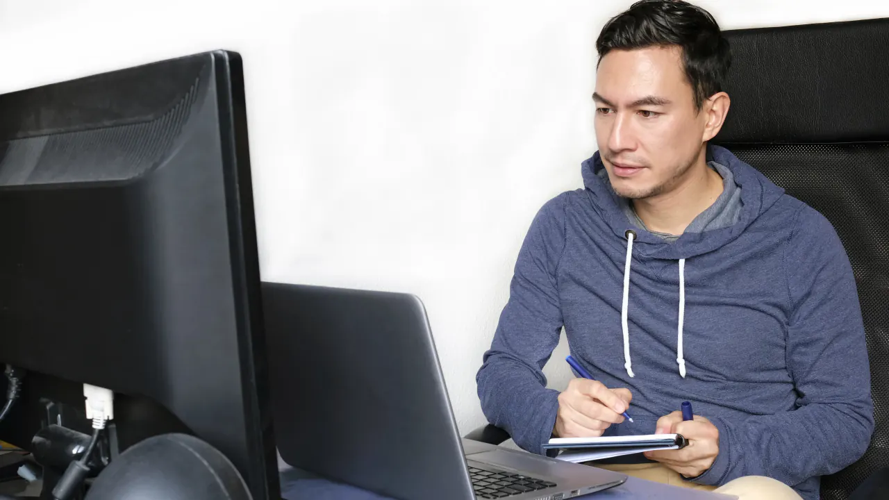 Man in a hoodie taking notes at a computer, illustrating a product qualified lead
