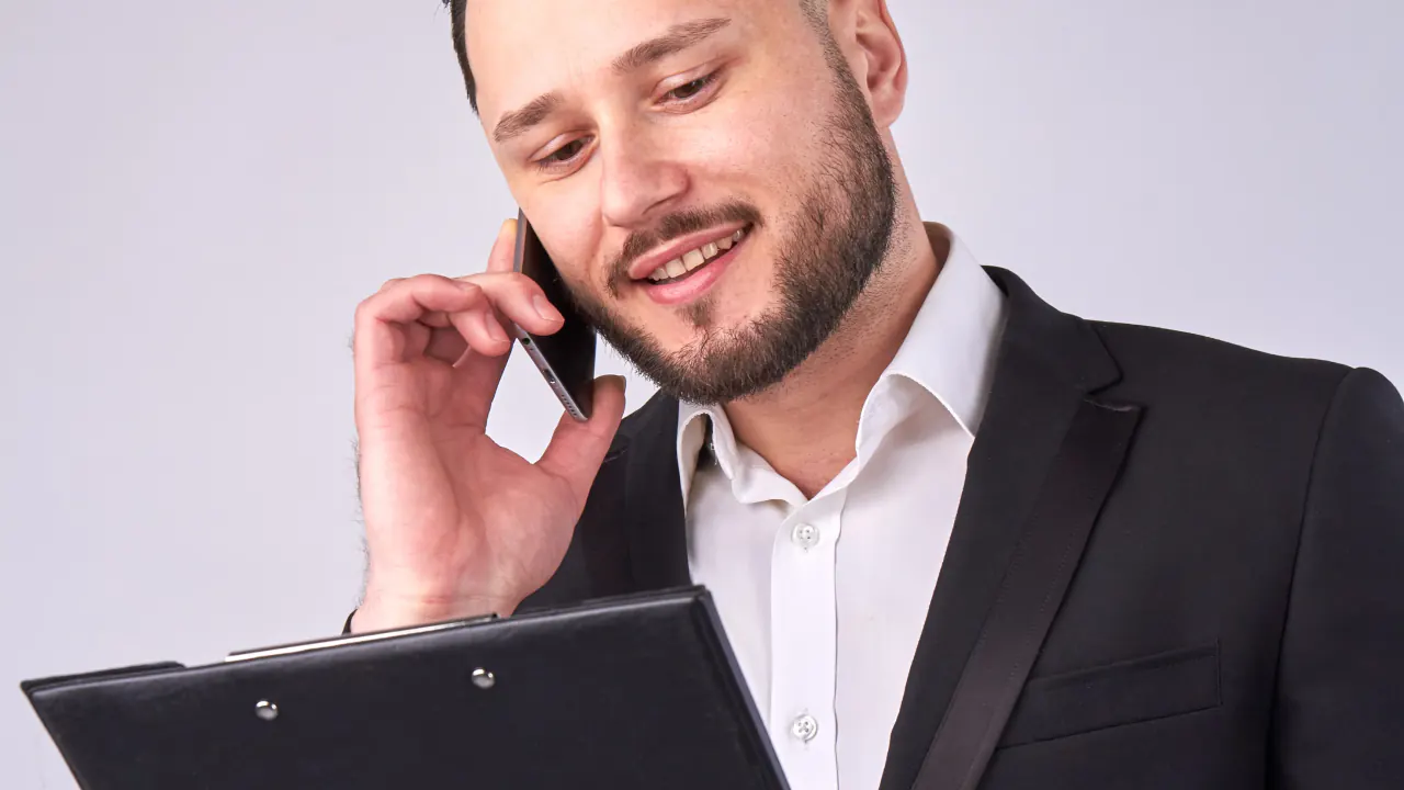 Smiling businessman on a phone call holding a clipboard, illustrating sales prospecting