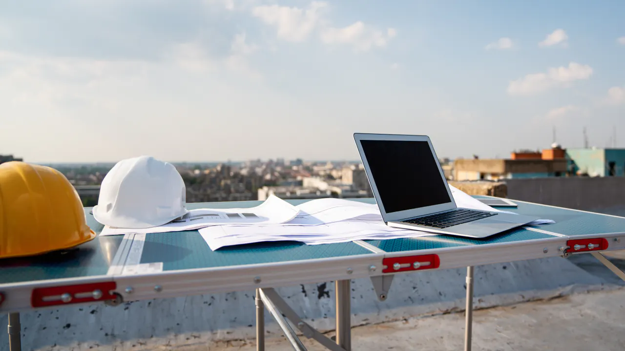 Hard hats, blueprints and a laptop on a rooftop table, illustrating appointment setting for commercial roofing contractors