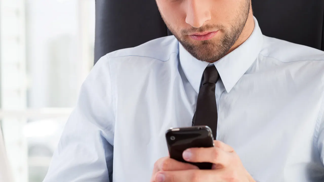 Businessman checking his phone at a desk, illustrating how to build a winning sales cadence