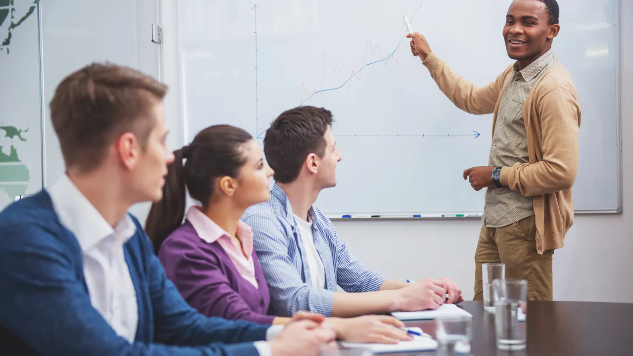 Presenter at a whiteboard teaching a sales team, illustrating sales enablement