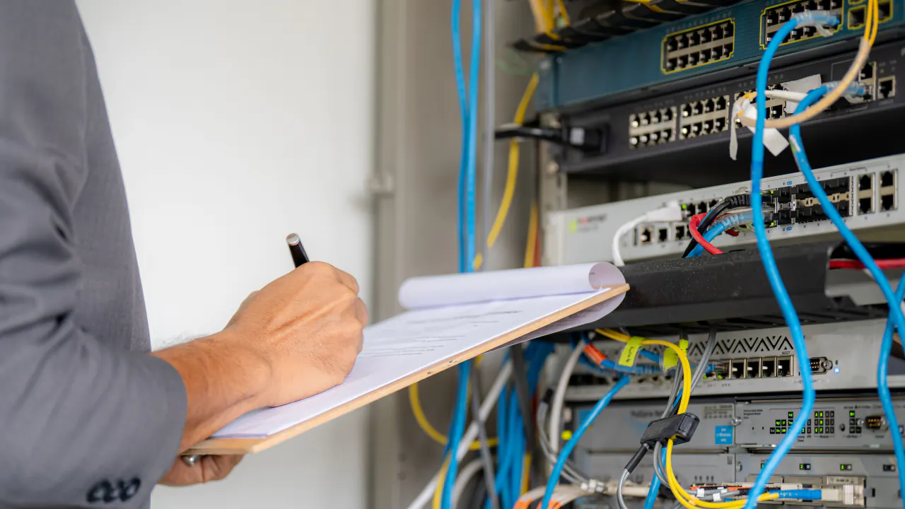 Technician taking notes beside a network server rack, illustrating B2B appointment setting for technology and telecom