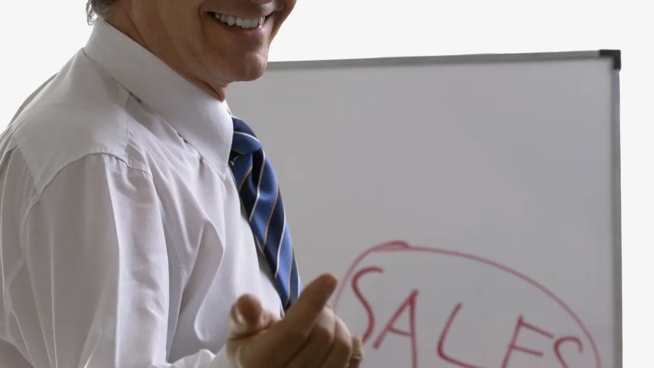 Sales trainer pointing at the word Sales on a whiteboard, illustrating a mock call exercise for sales reps