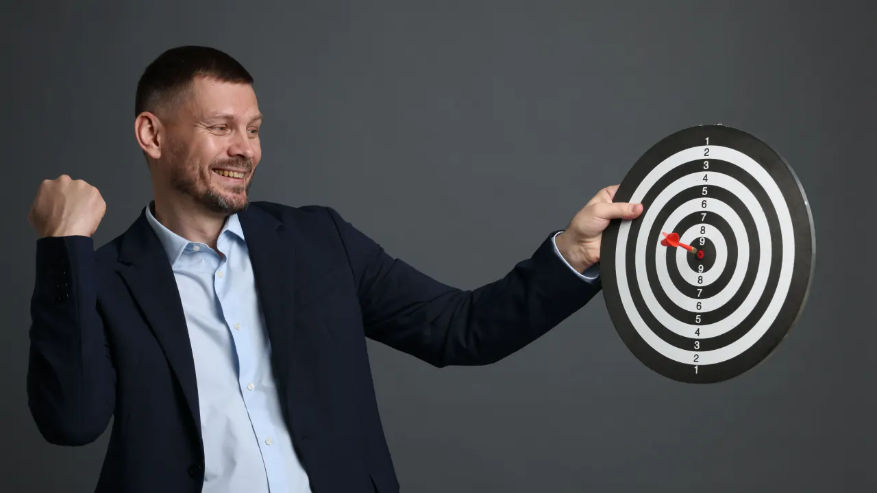 Smiling businessman hitting a dartboard bullseye, illustrating how to crush quotas in enterprise sales