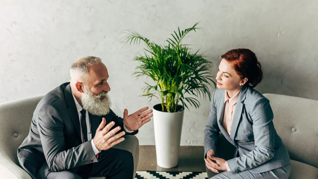Two professionals in conversation near a plant, illustrating the human proposition in sales